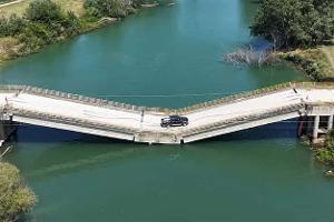 Eine Straßenbrücke, die in der Mitte zusammengebrochen ist, ist aus der Vogelperspektive zu sehen. Die Fahrbahn liegt knapp über einem Fluss und wird von einem Pickup befahren.