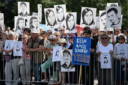 Zuschauer des Gedenkaktes der Landeshauptstadt München anlässlich des 10. Jahrestags des Attentats am Olympia-Einkaufszentrum halten Plakate mit Portraits der Opfer.