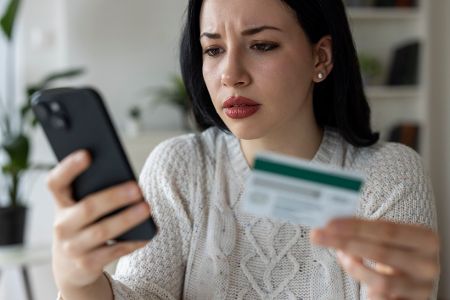 Frau mit Kreditkarte in der Hand schaut geschockt auf ihr Handy