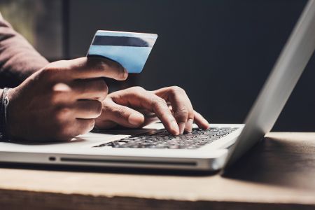 Person mit Kreditkarte in der Hand vor einem Laptop