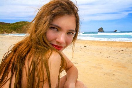 Eine Frau, deren Körper mit ihren langen Haaren verdeckt wird, sitzt am Strand