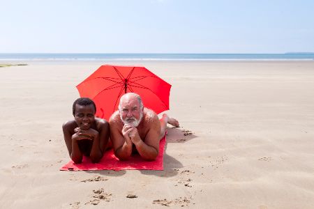 Eine schwarze Frau und ein weißer Mann liegen zusammen am Strand mit einem roten Sonnenschirm