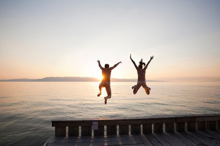 Zwei Nackte springen vom Steg in einen See bei Sonnenuntergang