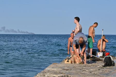 Menschen in Odessa sonnen sich, während am Horizont im Schwarzen Meer der brennende Getreidetransporter 
