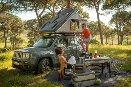 Zurück zur Natur: Prime Tech Delta Dachzelt zwischen hohen Bäumen, Leiter ausgeklappt, zwei Frauen genießen das Camping-Setup. Waldluft, Vogelgezwitscher und das Dach über dem Kopf – so schmeckt Freiheit.