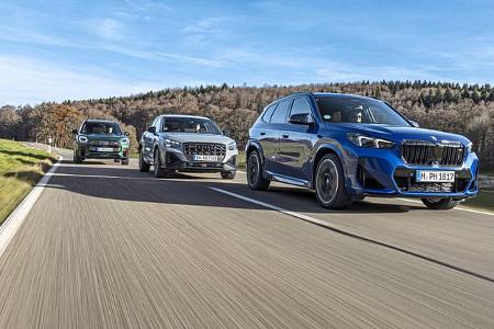 Drei Kompakt-SUVs – BMW X1 M35i xDrive, Audi SQ2 TFSI quattro S-tronic und Mini JCW Countryman 4all – fahren auf einer Landstraße nebeneinander. Die Fahrzeuge sind aus der Frontperspektive zu sehen, mit dem BMW X1 M35i im Vordergrund, dem Audi SQ2 in der Mitte und dem Mini JCW Countryman im Hintergrund. Die Szene spielt bei Tageslicht auf einer kurvigen Straße mit bewaldeter Landschaft.