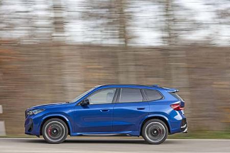 BMW X1 M35i xDrive in blauer Lackierung, fahrend auf einer Straße, Seitenansicht, Hintergrund mit Bewegungsunschärfe.