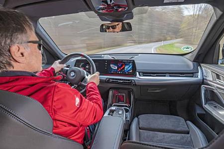 Innenraumaufnahme eines BMW X1 M35i xDrive während der Fahrt, Blick über die Schulter des Fahrers auf das Cockpit und die Straße.