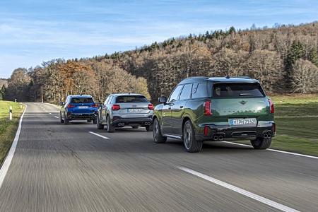 Drei Kompakt-SUVs – Audi SQ2, BMW X1 M35i xDrive und Mini JCW Countryman – fahren auf einer Landstraße durch eine herbstliche Landschaft.