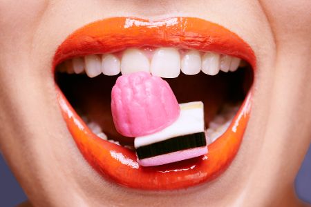 Frau mit rotem Lippenstift hält zwischen den Zähnen Süßigkeiten