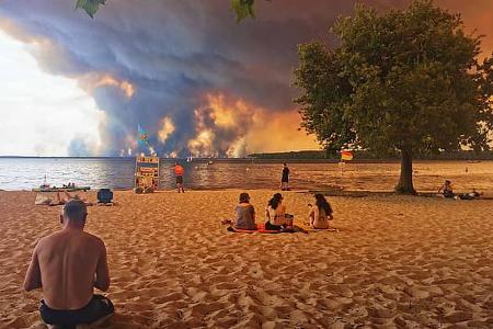TOPSHOT - Beach goers rest on the beach of Moutchic on the shore of Lake Lacanau (Etang de Lacanau) in Lacanau , southwestern France on July 24, 2026, as clouds of smoke rise into the sky from the Gironde wildfire. The fire raging in the northern part of the Arcachon Basin in Gironde, southwest France, has swept through more than 3,400 hectares, according to the latest figures released by the prefecture. More than 20,000 residents and tourists have been evacuated from this part already devastated by flames in 2022. Scientists have long warned that climate change caused by human use of fossil fuels will make periods of drought more intense and longer-lasting, creating the ideal conditions for wildfires. (Photo by Maximilien LAMY / AFP via Getty Images)