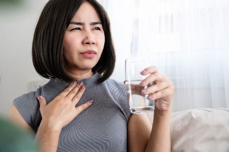Frau hält sich den Hals und trinkt ein Glas Wasser