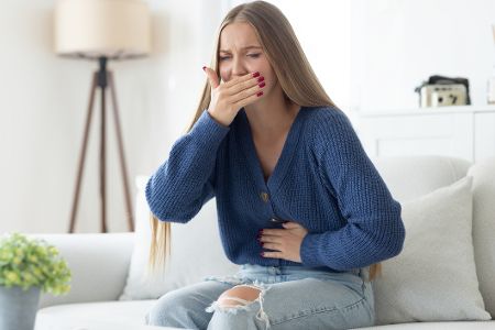 Frau hält sich mit einer Hand den Bauch, mit der anderen die Hand vor den Mund