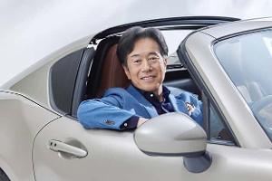 Ein Mann sitzt in einem hellen Mazda Cabrio, lehnt sich entspannt aus dem geöffneten Fenster und blickt freundlich in die Kamera.