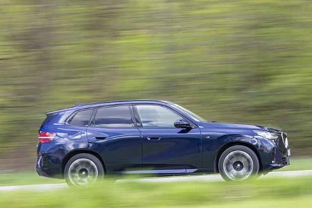 BMW X3 20 xDrive in blauer Lackierung, fahrend auf einer Landstraße vor unscharfem, grünem Hintergrund.