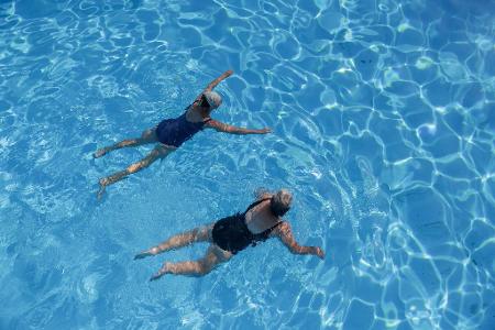 Zwei Frauen erfrischen sich in einem Außenbecken eines Schwimmbads. 