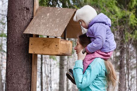 Mutter und ein Kind auf ihren Schultern schauen in eine Vogelhäuschen