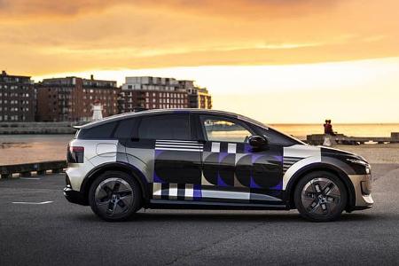 Audi A2 e-tron Erlkönig mit auffälliger Tarnfolierung an einer Uferpromenade bei Sonnenuntergang.