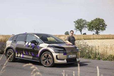 Audi A2 e-tron Erlkönig steht auf einer Landstraße vor einem Getreidefeld, daneben eine Person.