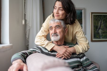 Frau umarmt liebevoll älteren Mann von hinten