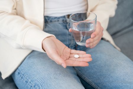 Frau hat eine Tablette in der einen, ein Glas Wasser in der anderen Hand