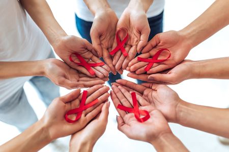Menschen stehen im Kreis und halten HIV-Schleifen in ihren Händen