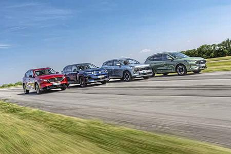 Vier aktuelle SUV-Modelle (Mazda CX-5, Citroen C5 Aircross Hybrid, Ford Kuga, Kia Sportage) fahren nebeneinander auf einer Landstraße oder Teststrecke bei Tageslicht. Die Fahrzeuge sind in unterschiedlichen Farben und aus schräger Frontansicht zu sehen, der Hintergrund zeigt eine grüne Landschaft und blauen Himmel.