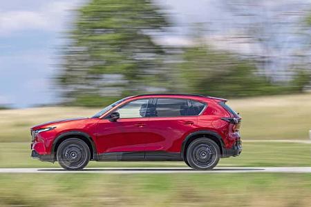 Mazda CX-5 2,5l E-Skyactive G fährt auf einer Landstraße, Seitenansicht, rote Lackierung, Bewegungsunschärfe im Hintergrund.