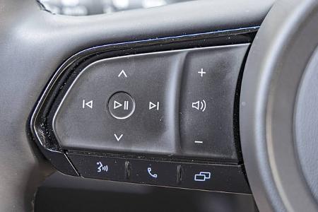 Detailaufnahme der Lenkrad-Bedientasten eines Mazda CX-5 2,5l E-Skyactive G. Die Tasten steuern Multimediafunktionen wie Lautstärke, Wiedergabe und Telefon.