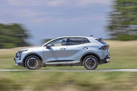 Kia Sportage 1,6 T-GDI SUV fährt auf Landstraße, Seitenansicht, in Bewegung, Sommerlandschaft im Hintergrund.