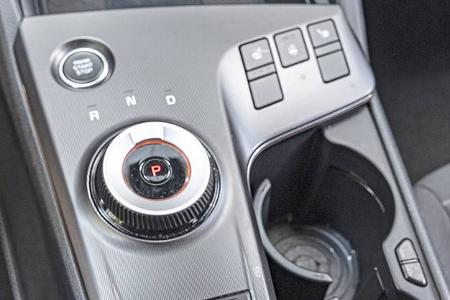 Detailaufnahme der Mittelkonsole eines Kia Sportage 1,6 T-GDI mit Drehregler für das Automatikgetriebe, Tasten für Sitzheizung und Getränkehalter.