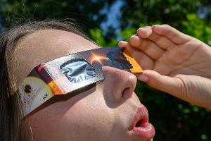 Eine junge Frau schaut durch eine Sonnenfinsternisbrille und betrachtet die Mittagssonne.