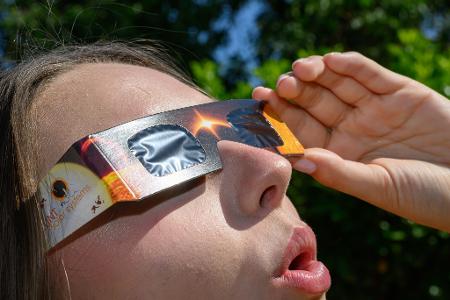 Eine junge Frau schaut durch eine Sonnenfinsternisbrille und betrachtet die Mittagssonne.