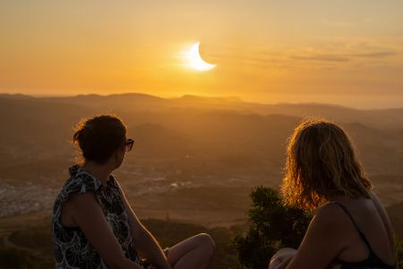 Zwei Frauen sitzen auf einem Berg über einer Stadt und schauen in den Sonnenuntergang