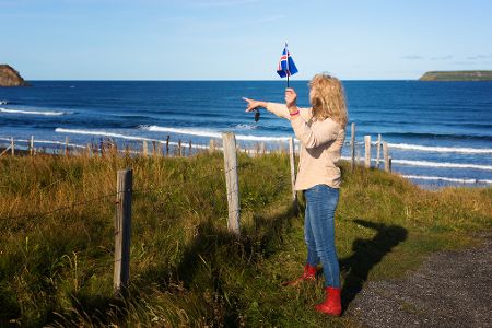 Frau mit Islandflagge in der Hand zeigt auf Küstenlinie