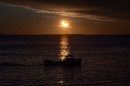 Partielle Sonnenfinsternis über dem Meer, im Vordergrund ein Kutter