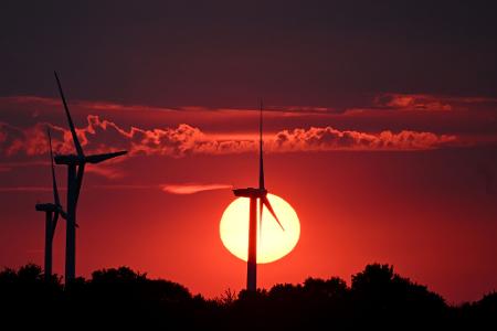 Hinter Windrädern färbt die sinkende Sonne den Himmel über Nordrhein-Westfalen rot. 