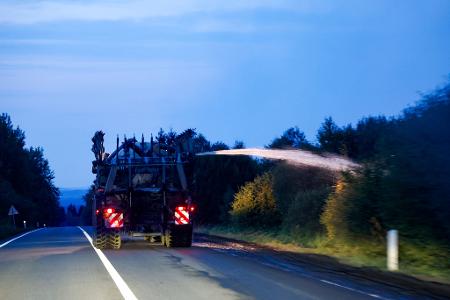 Ein landwirtschaftliches Fahrzeug wässert den Straßenrand mit Wasser aus dem Tank hinter seinem Traktor gegen die Flammen. 