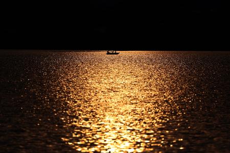Angler rudern in einem Kahn über den im Sonnenuntergang glitzernden Hopfensee.