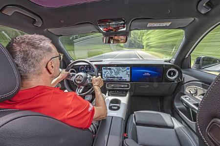 Innenraumaufnahme eines Mercedes GLB 250+ während der Fahrt, Blick über die Schulter des Fahrers auf das Cockpit und die Straße.