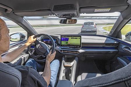Innenaufnahme eines Cupra Raval während einer Fahrszene auf dem Hockenheimring. Der Fahrer steuert das Fahrzeug, das digitale Cockpit und das zentrale Infotainment-Display sind deutlich sichtbar. Vor dem Fahrzeug fährt ein weiteres Auto auf der Rennstrecke.