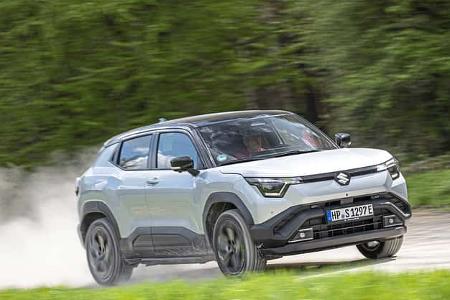 Suzuki e-Vitara eAxle SUV fährt dynamisch auf einer Landstraße, im Hintergrund grüne Vegetation.