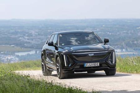 Cadillac Lyriq-V fährt auf einer Landstraße mit Stadt und Fluss im Hintergrund.