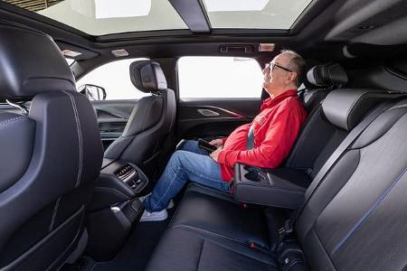 Innenaufnahme des Cadillac Lyriq-V, Blick auf die Rücksitzbank mit einer Person, die auf dem rechten Rücksitz Platz genommen hat. Das große Panoramaglasdach und die hochwertigen Ledersitze sind deutlich sichtbar.