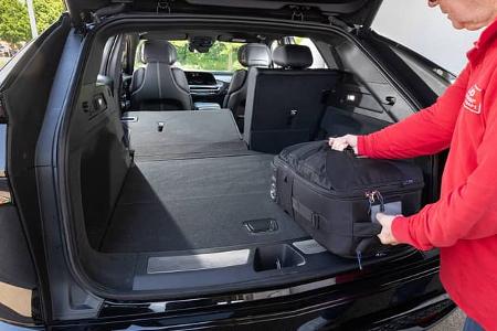 Der geöffnete Kofferraum eines Cadillac Lyriq-V mit umgeklappter Rückbank. Eine Person legt eine schwarze Tasche in den Laderaum.