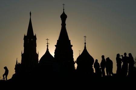 Menschen spazieren bei Sonnenuntergang im Zaryadye-Park in Moskau vor dem Hintergrund des Spasskaja-Turms des Kremls und der Basilius-Kathedrale.