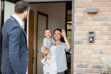 Mutter mit Baby auf dem Arm winkt dem Vater, der zur Arbeit geht