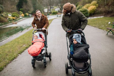 Zwei Väter gehen mit ihren Babys im Kinderwagen spazieren