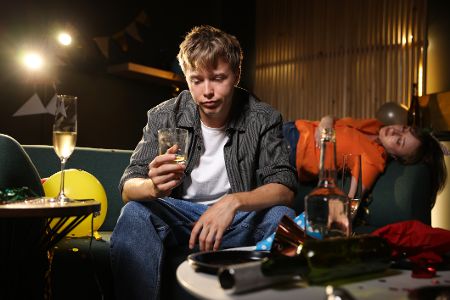 Junger Mann sitzt betrunken und benommen auf einer Couch auf einer Party