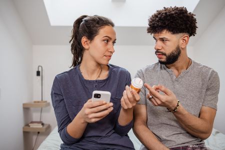 Mann und Frau sitzen zusammen und haben Pillendose und Handy in der Hand